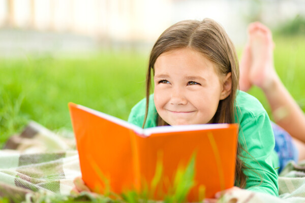拿着书本趴在草地上的小女孩图片