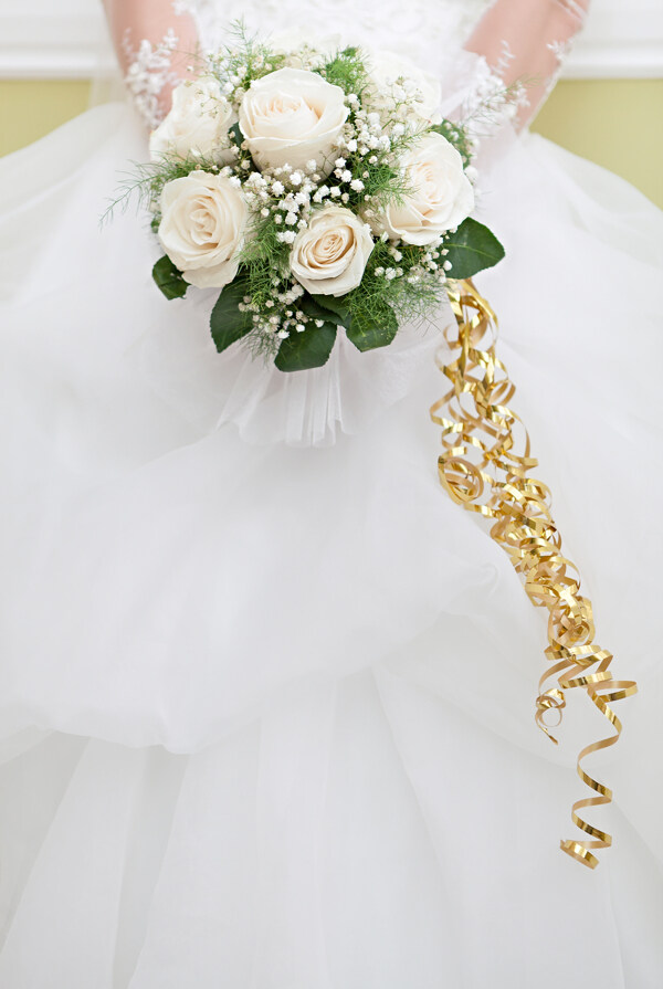白色婚纱上拿着捧花的新娘的手图片
