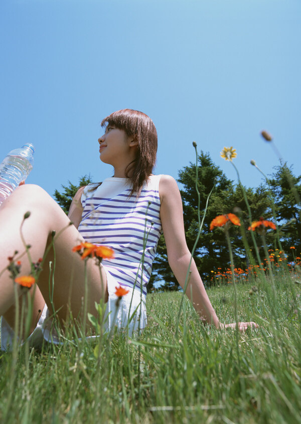坐在草地上喝水的美女图片